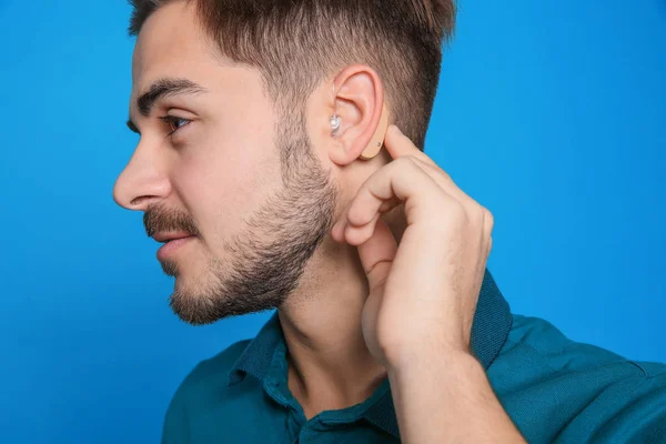 Jovem Homem Ajustando Aparelho Auditivo Fundo Cor — Fotografia de Stock