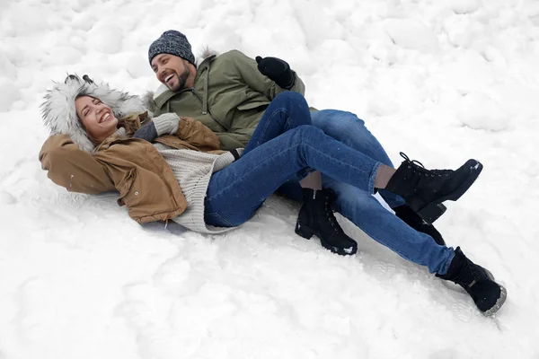 Happy couple lying on snow outdoors. Winter vacation