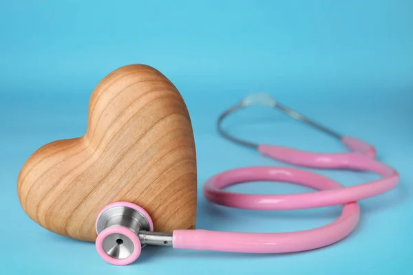 Stethoscope with wooden heart on blue background, closeup. Space for text