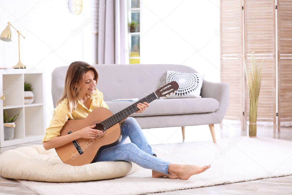 Young woman playing acoustic guitar in living room