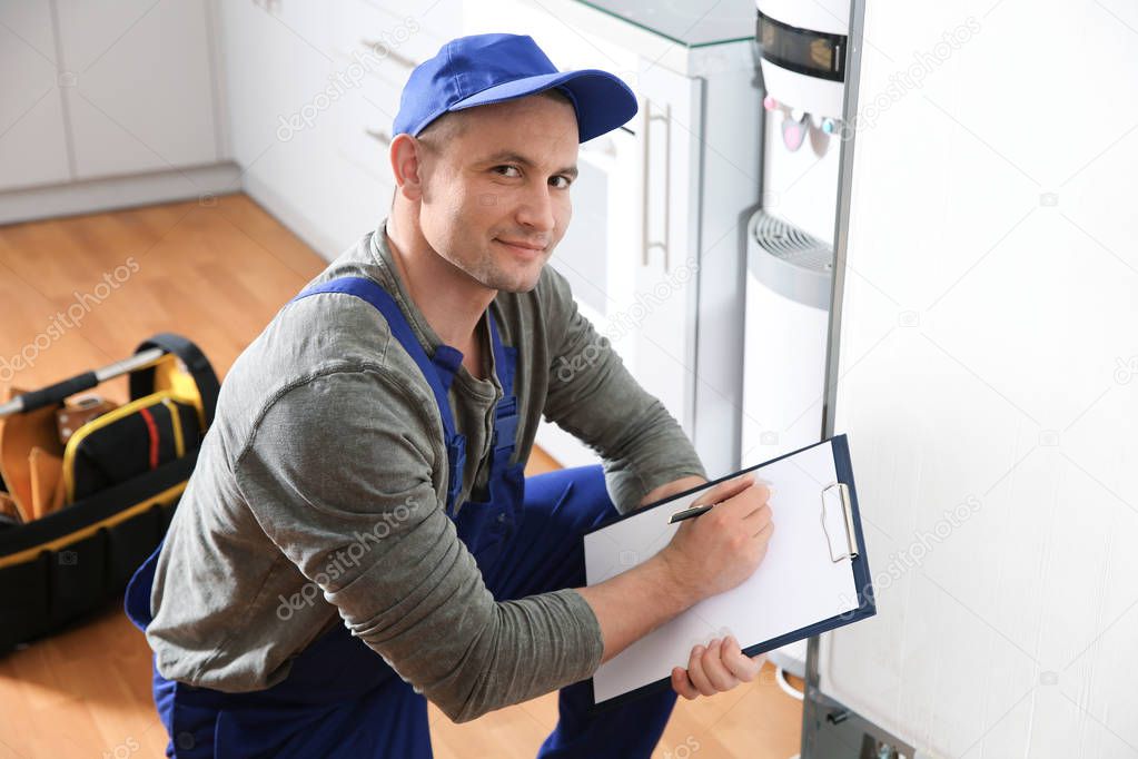 Male technician with clipboard examining broken refrigerator in kitchen