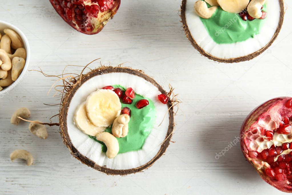 Flat lay composition with yummy spirulina smoothie in coconuts and pomegranate on wooden background