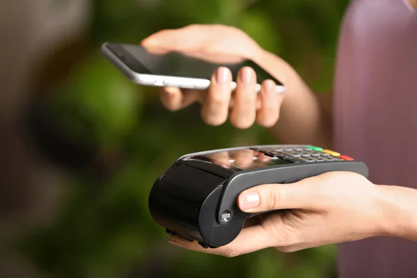 Woman using modern payment terminal with mobile phone indoors, closeup