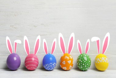 Paskalya yumurtaları ve sevimli tavşan'ın kulakları ahşap arka plan karşı masada dekore edilmiştir. Metin için yer 