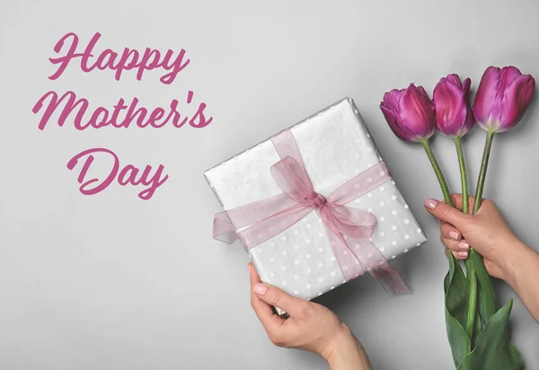 Woman holding gift and tulips on light background, top view. Happy Mother\'s Day