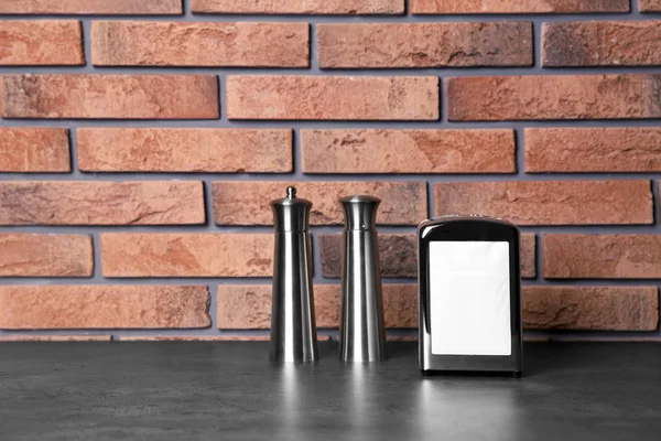 Napkin holder with salt and pepper shakers on table against brick wall. Space for text