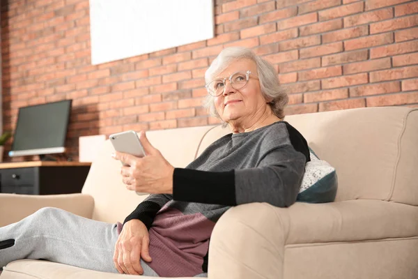Elderly woman using smartphone on sofa in living room