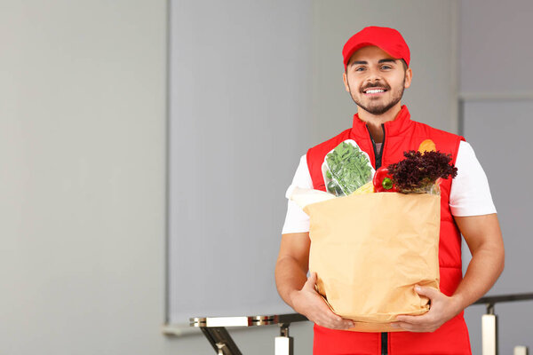 Food delivery courier holding paper bag with products indoors. Space for text