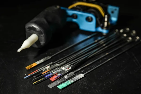 Tattoo needles covered with colorful inks on black background