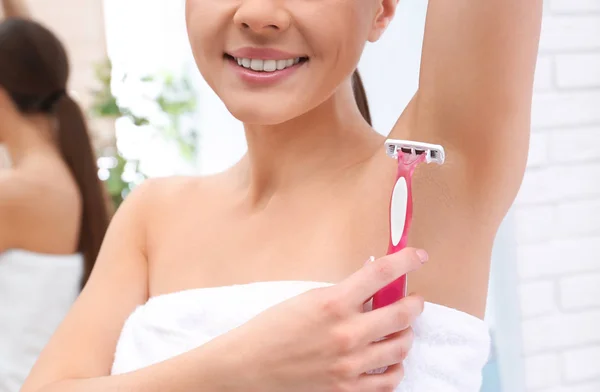 Beautiful young woman shaving armpit at home, closeup