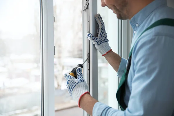 Construction worker adjusting installed window with screwdriver indoors, closeup