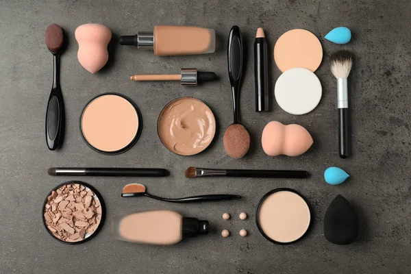 Flat lay composition with skin foundation, powder and beauty accessories on grey background