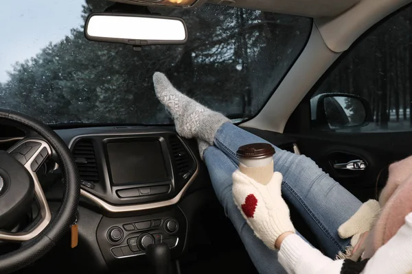 Woman in warm socks with coffee resting inside car, closeup