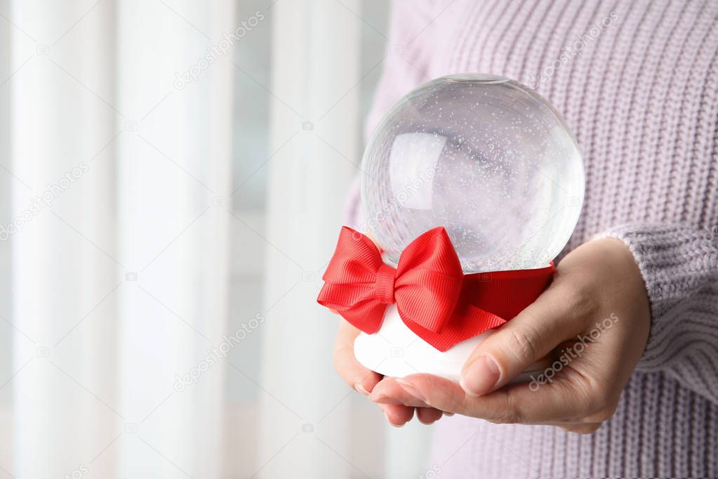Woman holding empty snow globe with red bow indoors, closeup. Space for text