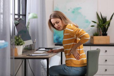 Young woman suffering from back pain in office clipart