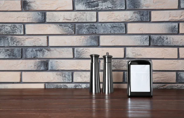 Napkin holder with salt and pepper shakers on table against brick wall. Space for text