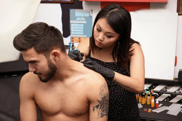 Professional artist making tattoo with machine in salon