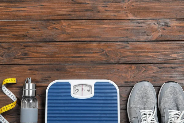 Flat lay composition with scales, sneakers, sport bottle and space for text on wooden background, top view. Weight loss