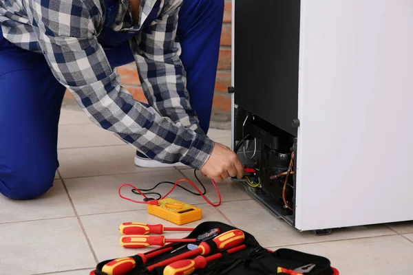 Male technician repairing broken refrigerator indoors, closeup