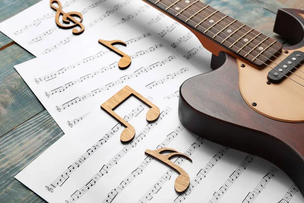 Guitar and sheets with music notes on wooden table