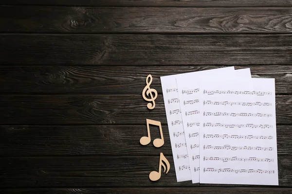 Sheets and music notes on wooden background, top view. Space for text