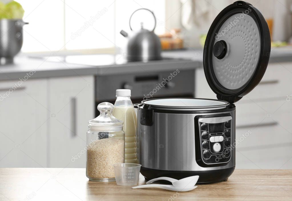 Modern electric multi cooker, rice and milk on table in kitchen. Space for text