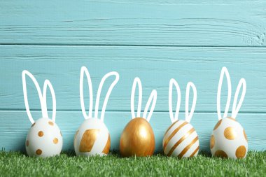 Paskalya yumurtaları ve sevimli tavşan'ın kulakları ahşap arka plan karşı yeşil çimlerin üzerine dekore edilmiştir. Metin için yer 