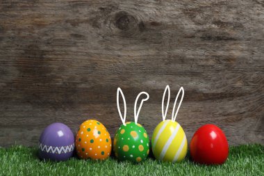 Paskalya yumurtaları ve sevimli tavşan'ın kulakları ahşap arka plan karşı yeşil çimlerin üzerine dekore edilmiştir. Metin için yer 