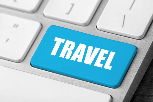 Computer keyboard with blue button and word Travel. Tourist agency