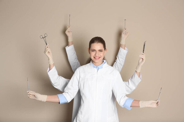Female dentist with multiple hands holding tools on color background