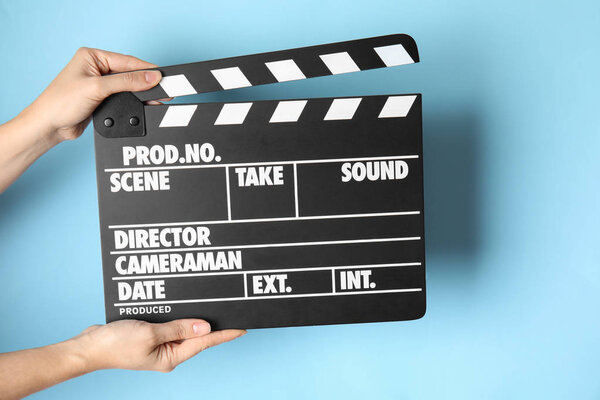 Woman holding clapperboard on color background, closeup. Cinema production