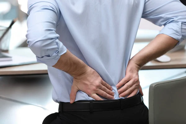 Businessman suffering from back pain at workplace, closeup