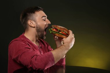 Genç adam renk arka plan üzerinde lezzetli hamburger yeme. Metin için yer