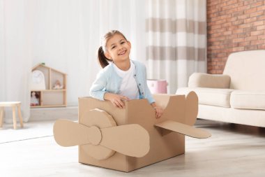 Oturma odasında karton uçak ile oynayan sevimli küçük kız
