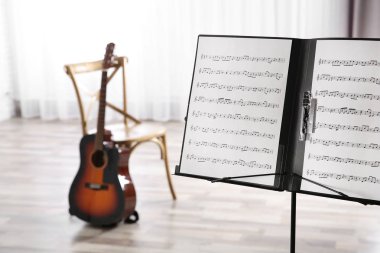 Müzik sayfaları ve arka plan üzerinde bulanık akustik gitar ile Not stand. Metin için yer