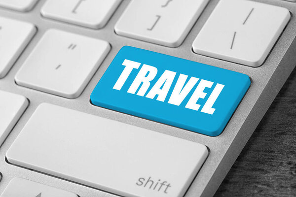 Computer keyboard with blue button and word Travel. Tourist agency