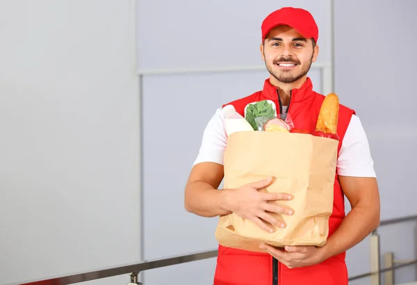 Food delivery courier holding paper bag with products indoors. Space for text