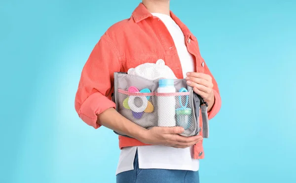 Woman holding maternity bag with baby accessories on color background, closeup