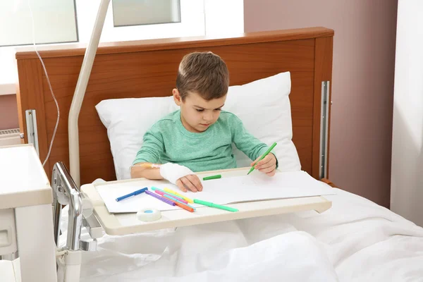 Little child with intravenous drip drawing in hospital bed
