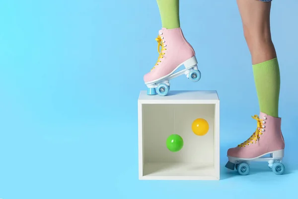 Woman wearing vintage roller skates near storage cube with balls on color background, closeup. Space for text