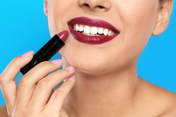 Young woman applying lipstick on color background, closeup