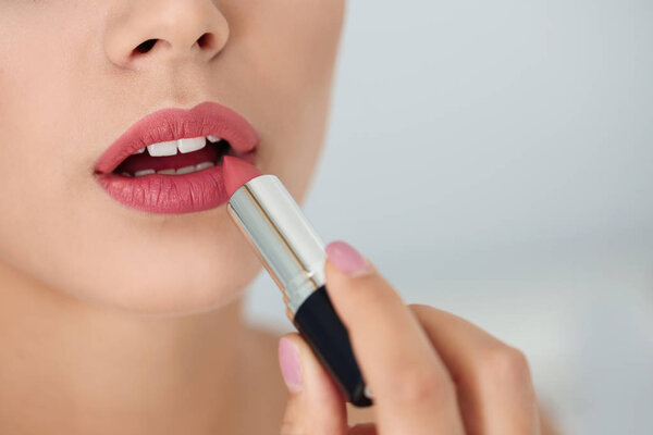 Young woman applying lipstick on light background, closeup