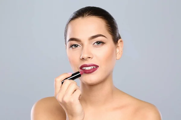 Mujer Joven Aplicando Lápiz Labial Sobre Fondo Color —  Fotos de Stock