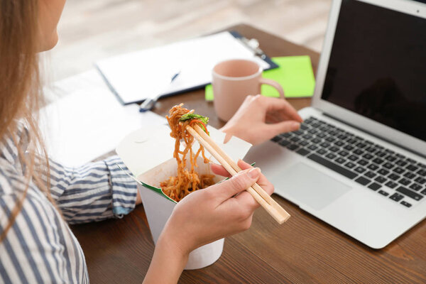Office employee using laptop while having noodles for lunch at workplace, closeup. Food delivery