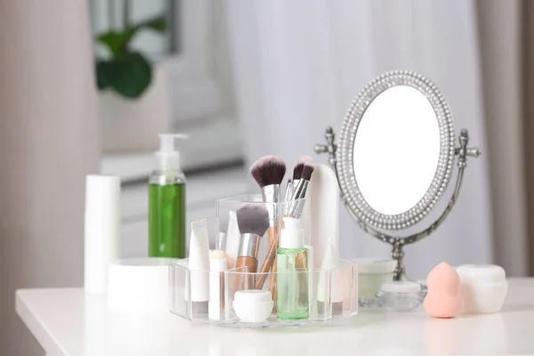 Cosmetic products and makeup accessories on table against blurred background