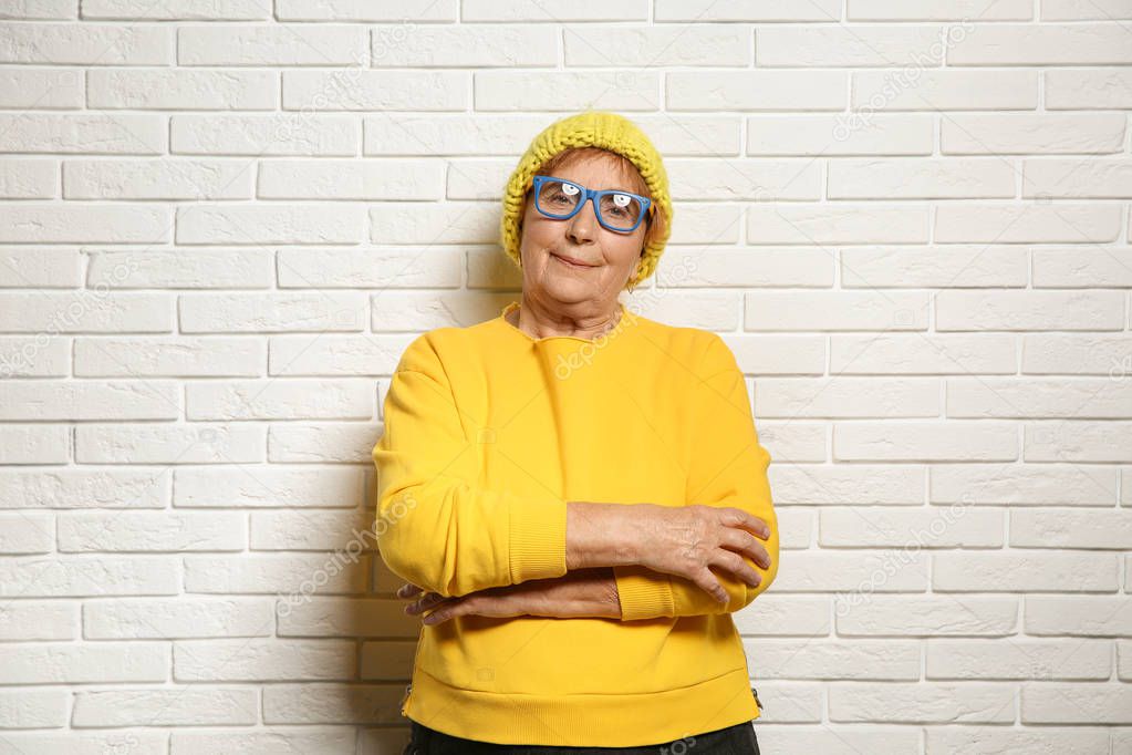 Portrait of elderly woman in hipster outfit near brick wall
