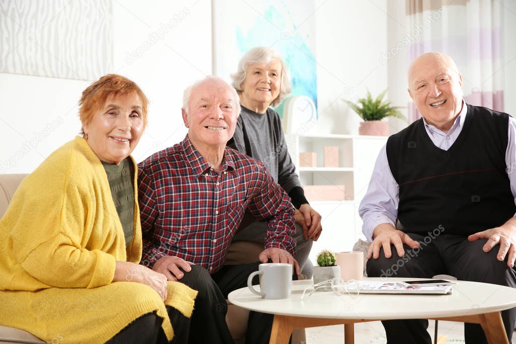 Portrait of happy elderly people at table in living room