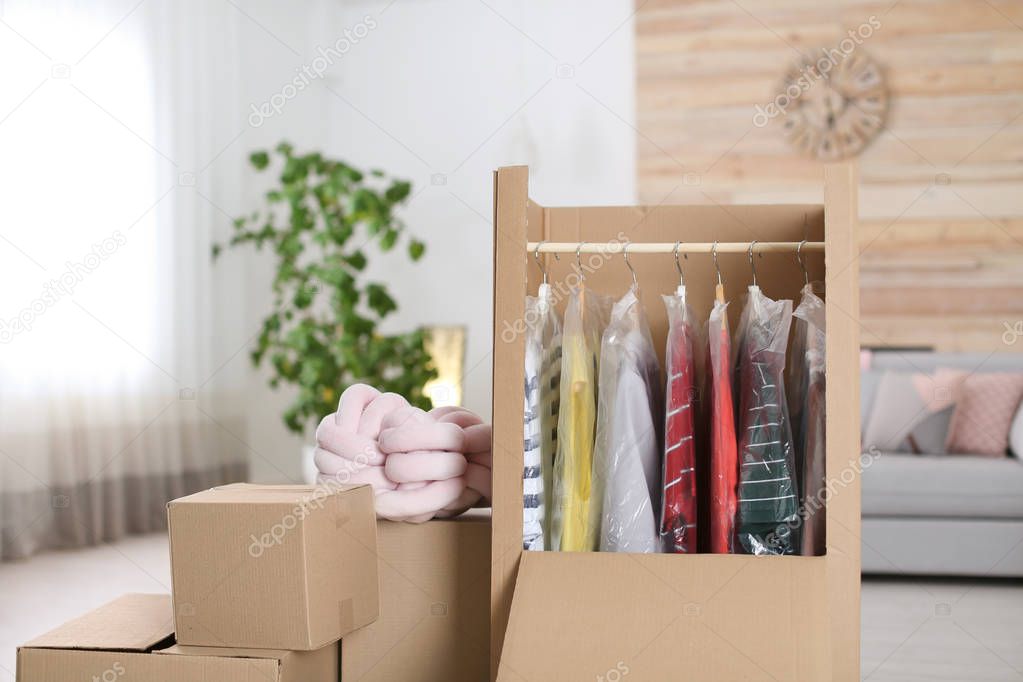 Cardboard wardrobe box with clothes on hangers in living room