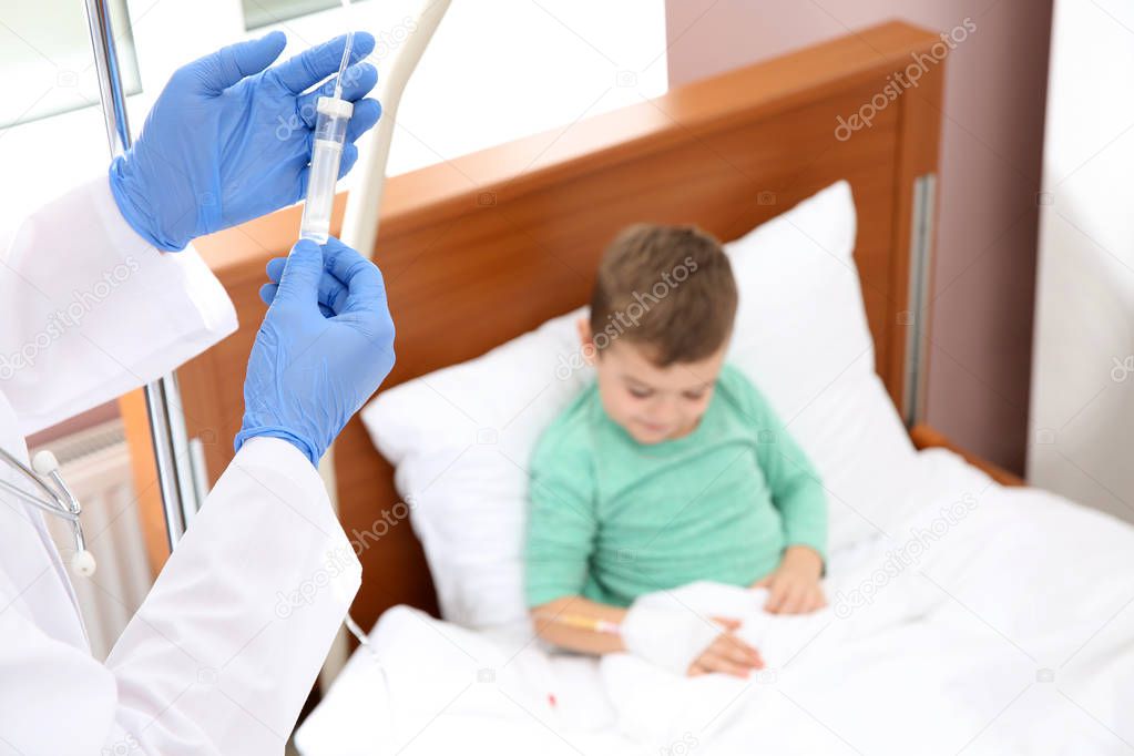 Doctor adjusting intravenous drip for little child in hospital, closeup