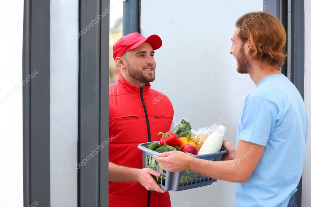 Courier giving plastic crate with products to customer at home. Food delivery service